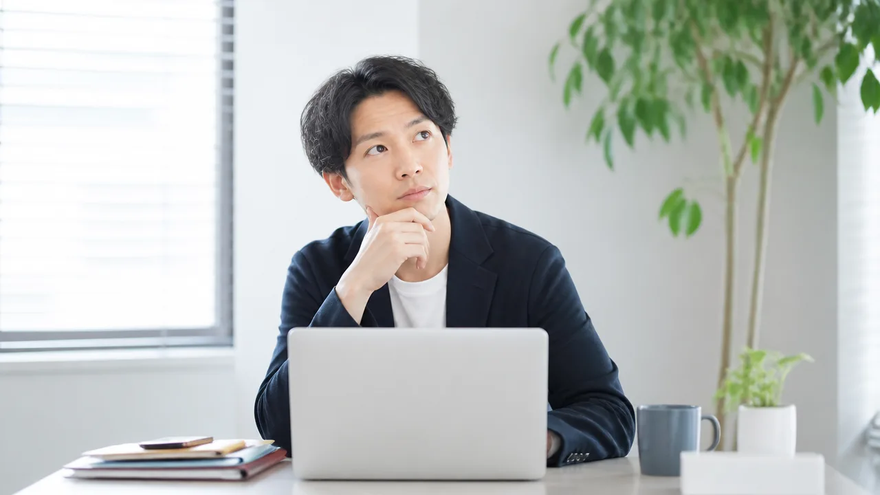 ノートパソコンの前で、勤務時間について考える人のイメージ