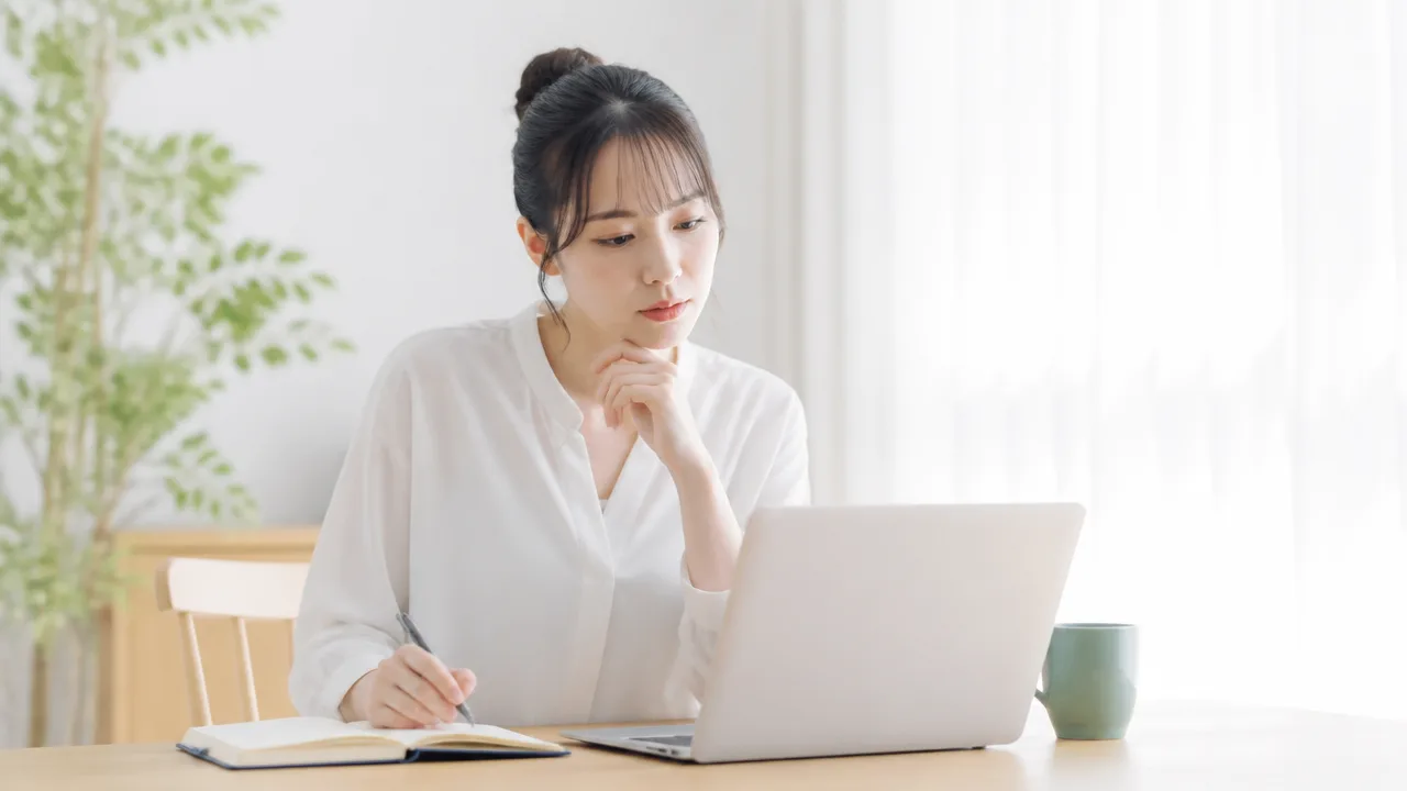 ノートパソコンを見ながらノートに確認事項を書き留める人のイメージ