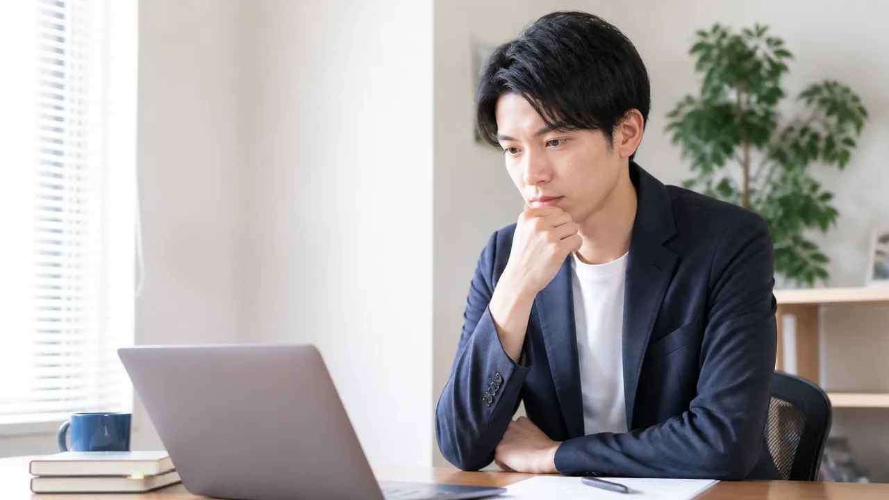 パソコンと書類を前に考える人のイメージ